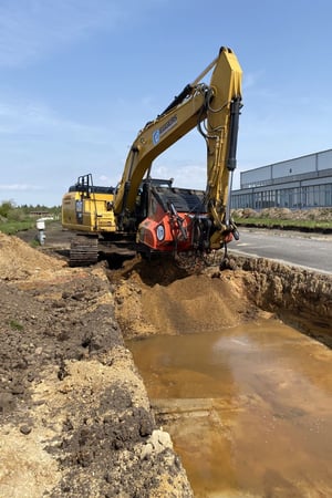 Kampfmittelbergung in Leck (Schleswig-Holstein): CAT 326F mit Minebuster siebt kampfmittelverdächtigen Boden an einem wassergefüllten Suchschnitt.