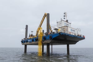 Jack-Up-Barge „Helgoland“ der EGGERS Kampfmittelbergung. Arbeitsplattform mit Marine-Service-Containern und abgesenkten Stelzen für Kampfmittelsondierung in der Nordsee bei Wilhelmshaven.