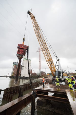 Hydroseilbagger mit Vibrationsramme zieht einen Stahlträger/Spundbohle an der ehemaligen Rethebrücke in Hamburg-Wilhelmsburg; Rückbauarbeiten auf dem Wasser mit begleitender Kampfmittelsondierung.